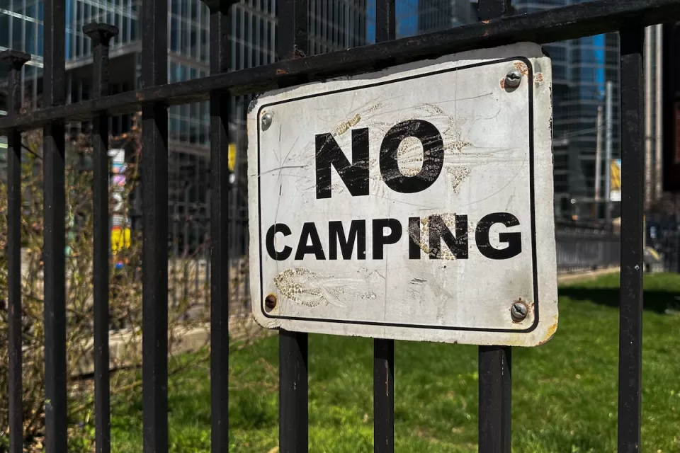 Close-up of white and black NO CAMPING sign on black iron fence.
